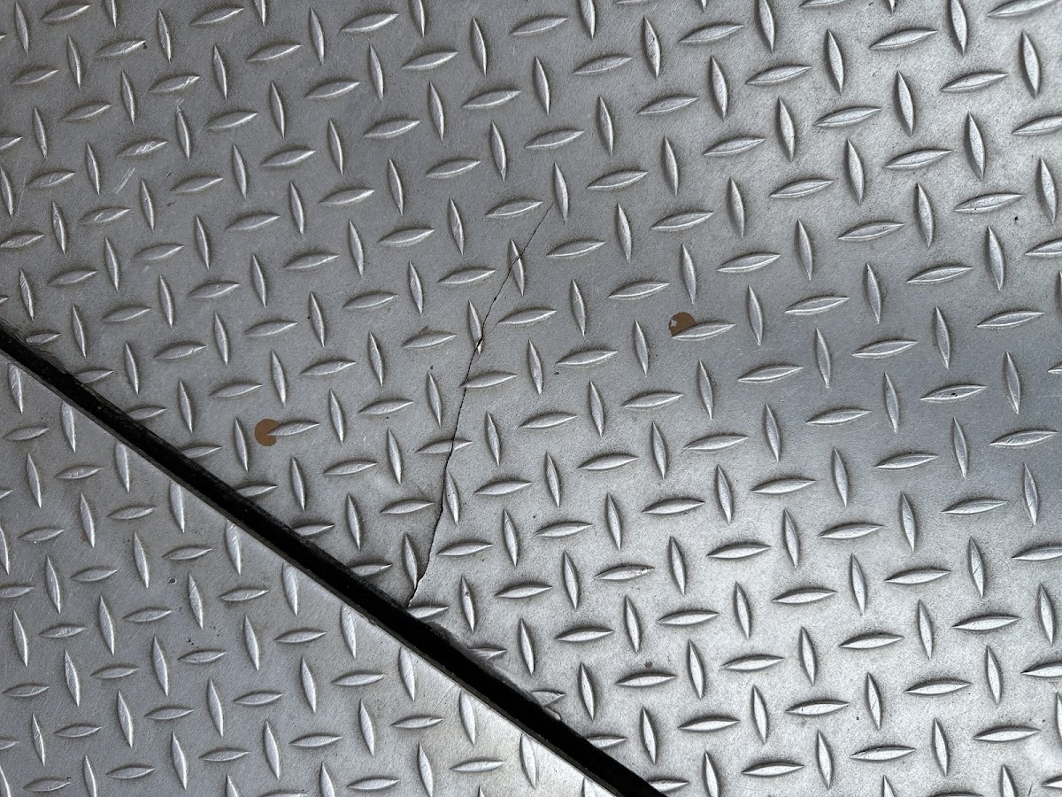 Close-up of diamond-plate steel with a repaired weld seam along a crack