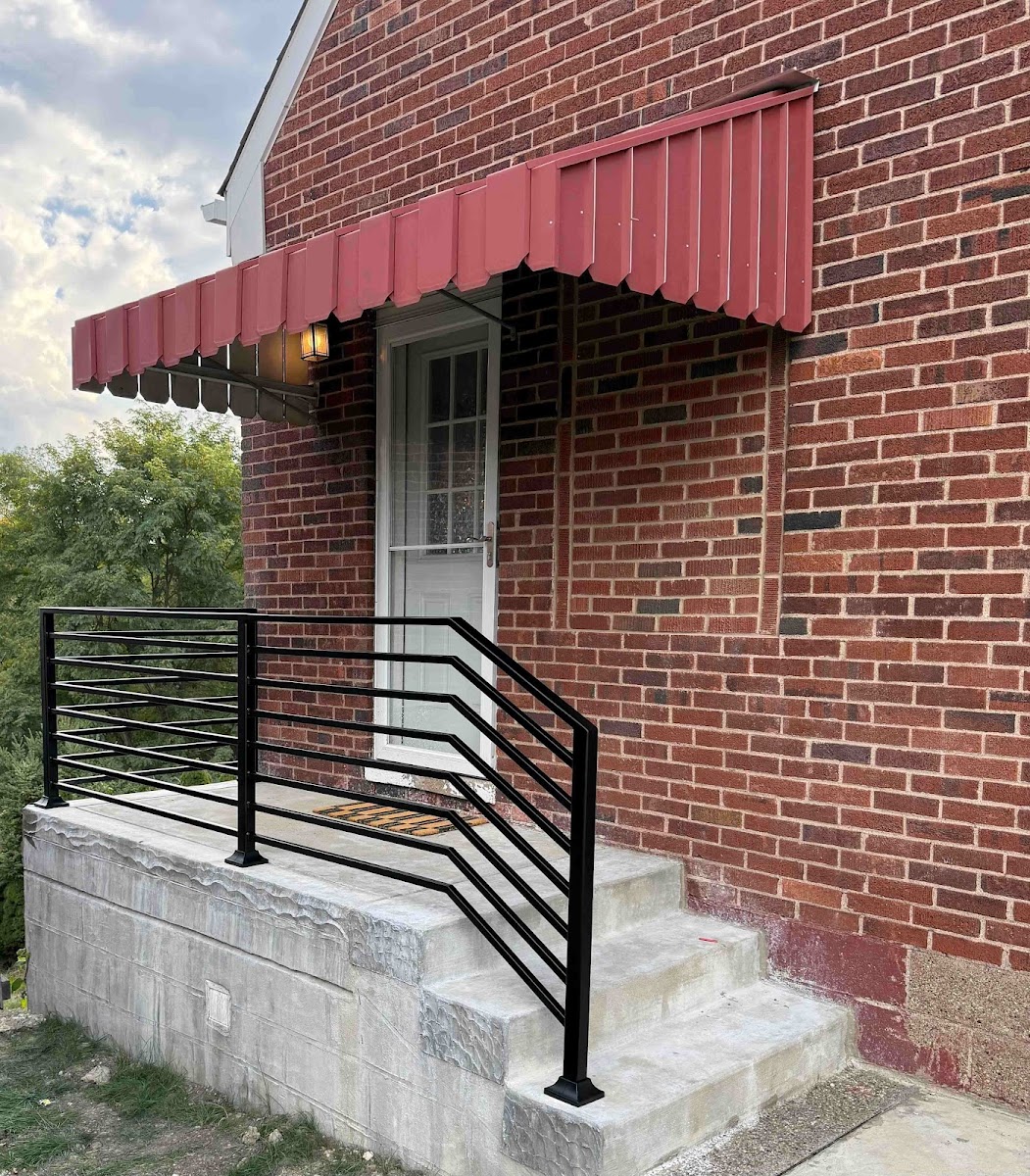 A simple black horizontal-bar iron railing installed on a brick rowhouse porch with a red awning