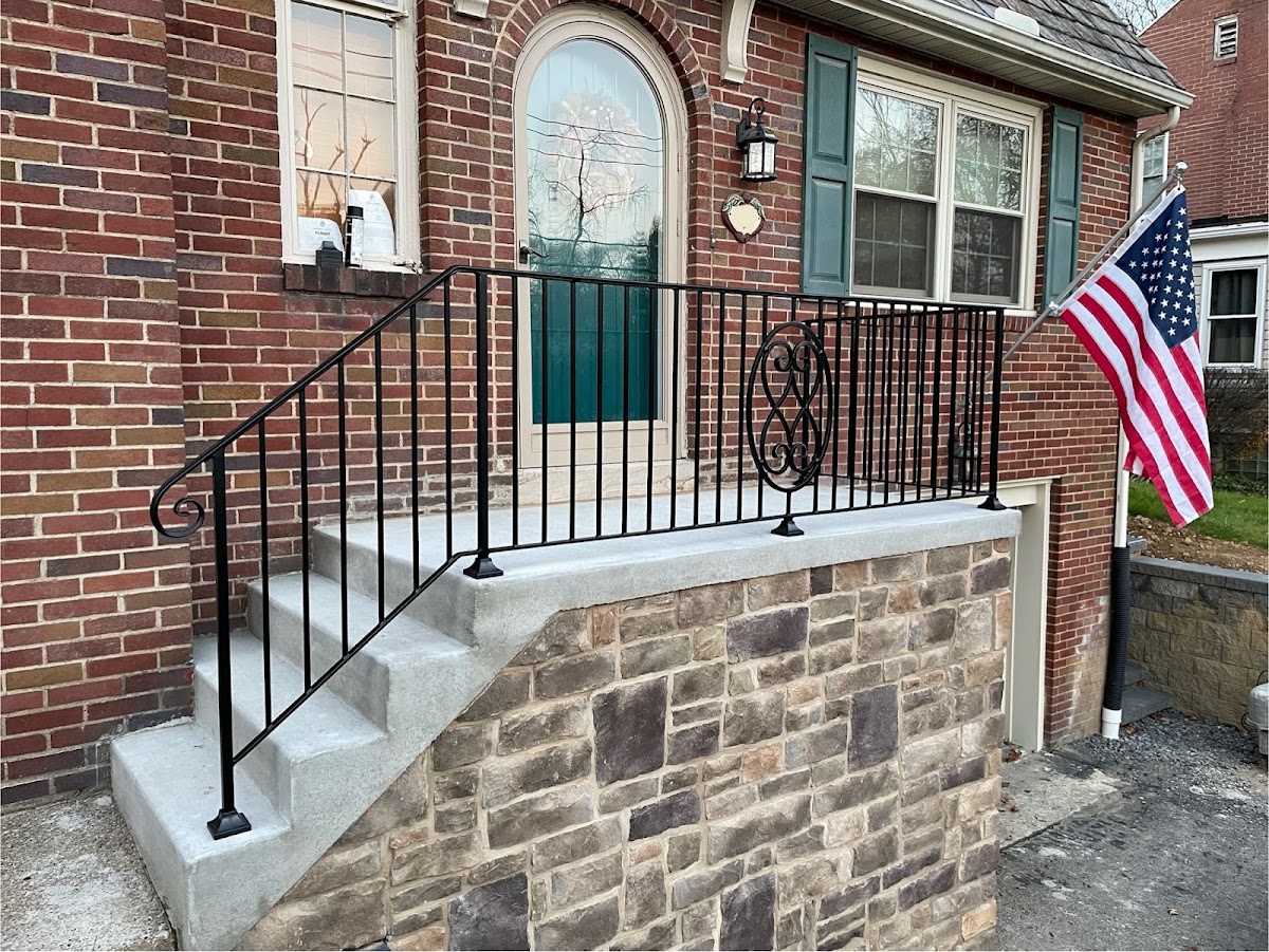 A custom black iron stair railing with a scrollwork medallion, installed on a brick Pittsburgh home